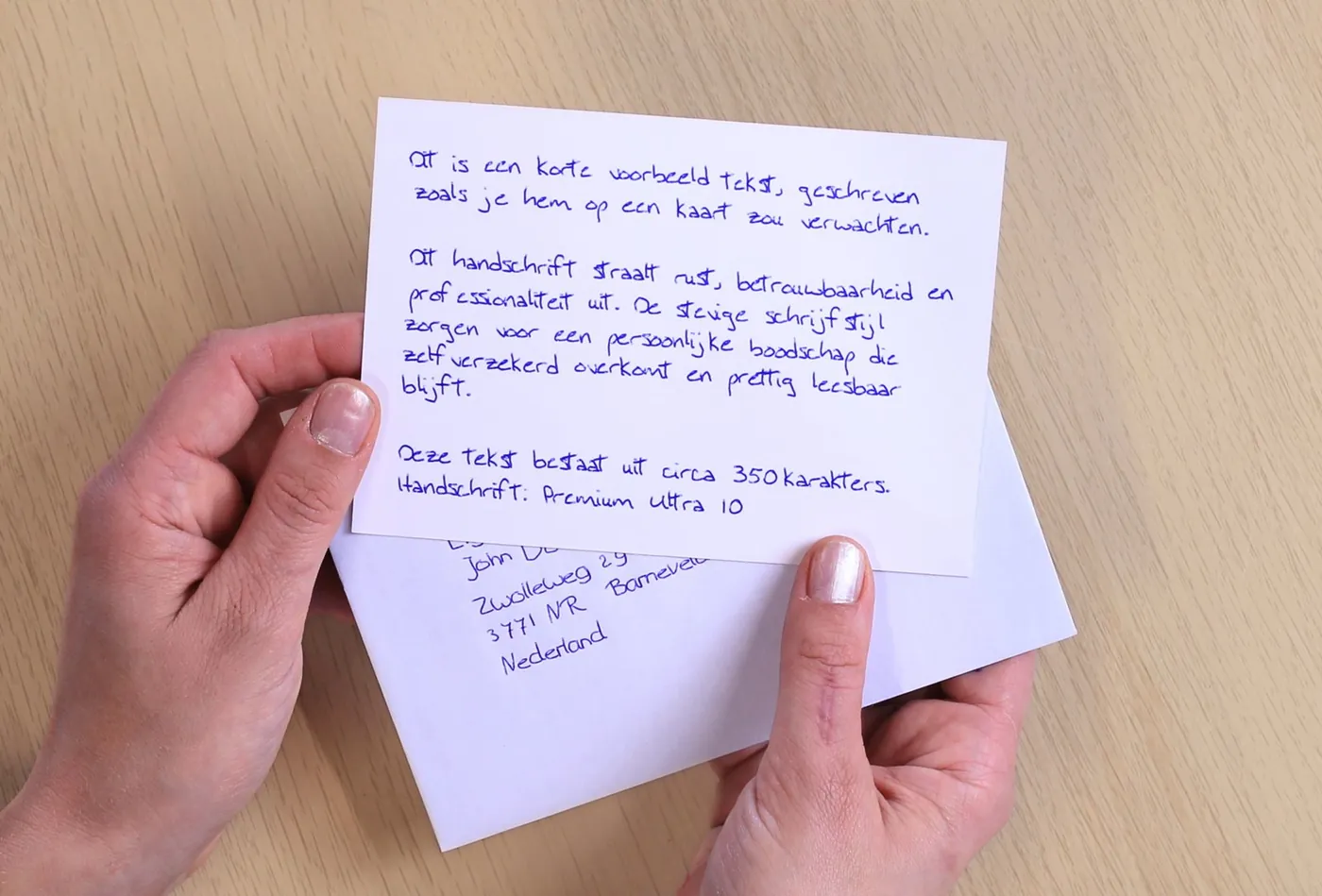 Twee handen houden een geschreven kaart vast boven een envelop met een met de pen geschreven adres